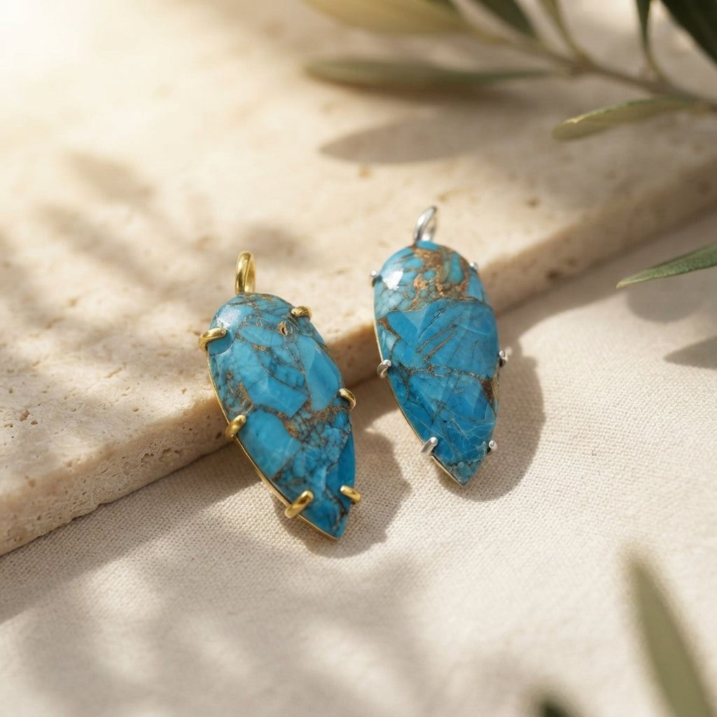 Two turquoise gemstone pendant necklaces in gold and silver settings, laid on a natural travertine stone surface.